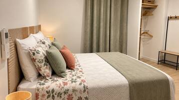 Ein ordentlich bezogenes Bett mit Blumenmuster, eine Nachttischlampe und ein Holfnachttisch.