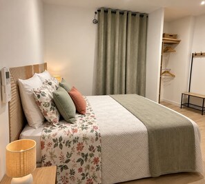 Een opgemaakt bed met bloemenbeddengoed, een bedlampje en een houten nachtkastje.
