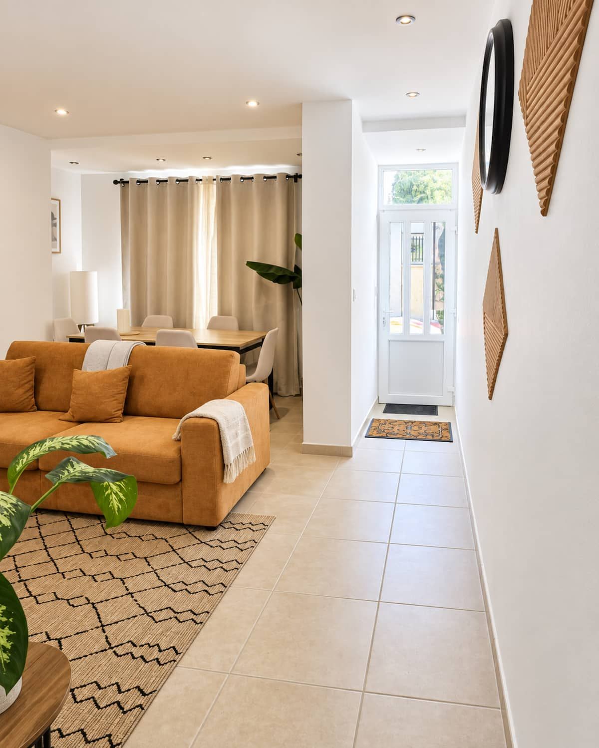 A modern living room with a sofa, a dining table with chairs, and a view of the outdoors.