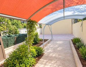 A covered outdoor area with a curved roof, a concrete pathway, and various plants. - L’Escale de Montélimar – Air-conditioned duplex, walk to station & parking (Montélimar)