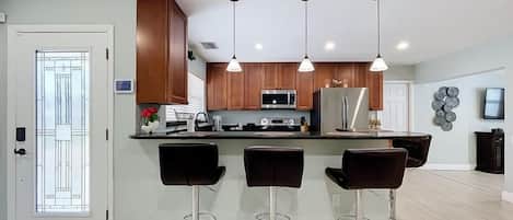 A modern kitchen with a central island, bar stools, and pendant lighting.