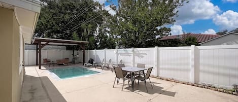 Un jardin avec une piscine, des meubles de patio et un espace salon abrité.
