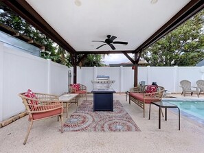 Eine Außenpatio mit Deckenventilator, Grill und Schwimmbecken.