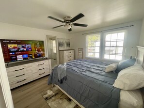 A bedroom with a bed, a TV mounted on a dresser, a ceiling fan, and a window with blinds. - HPU Perfect New House (High Point)