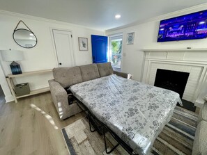 A room with a sofa, a bed with a floral bedspread, a television, and a fireplace. - HPU Perfect New House (High Point)