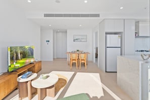 A modern living room with a flat-screen TV, a wooden coffee table, and a dining area with a table and chairs. - Luxury 2BR with Panoramic Gold Coast Views (Broadbeach)