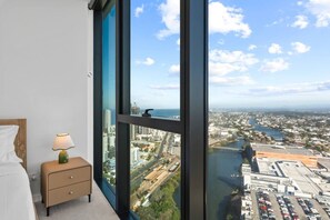 Ein Schlafzimmer mit großem Fenster, einer Nachttischlampe und Blick auf Stadt und Wasser.