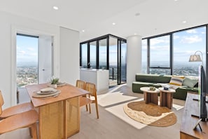 A modern apartment with a dining area, a living room with a green sofa, and large windows offering a city view. - Luxury 2BR with Panoramic Gold Coast Views (Broadbeach)
