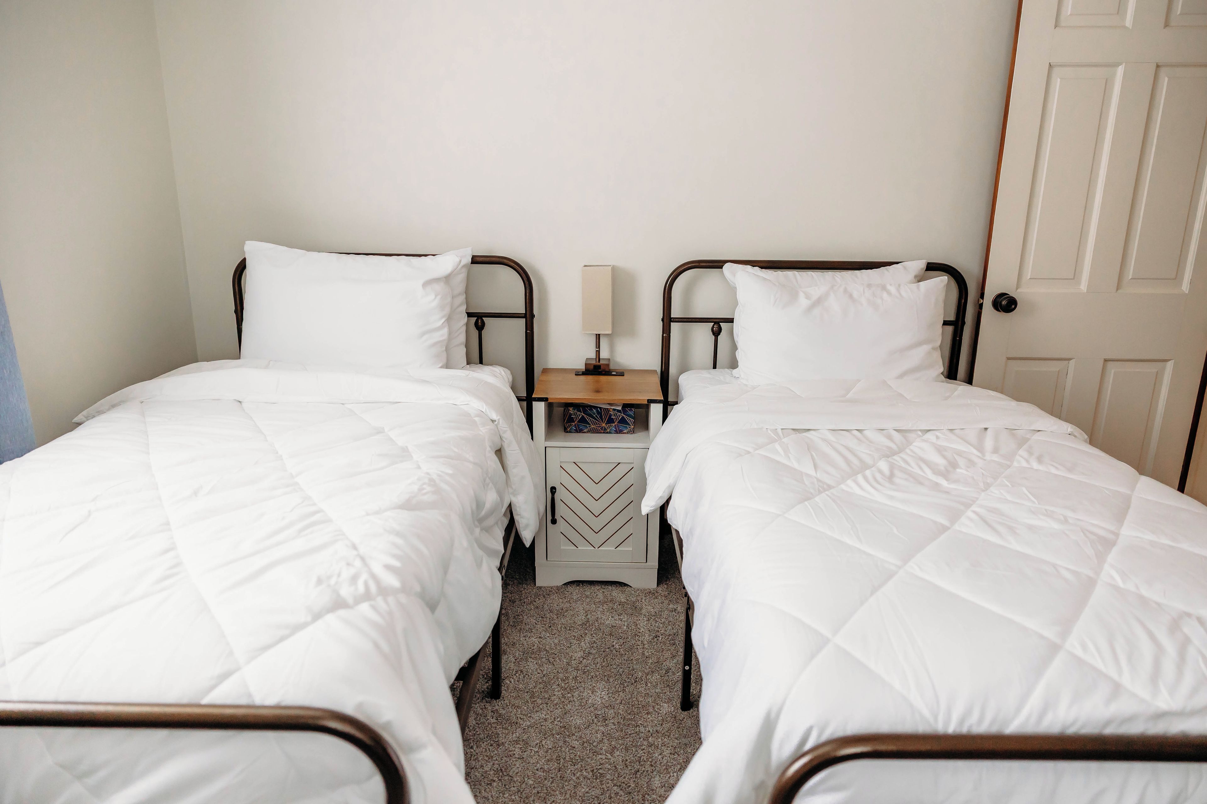 Ein Doppelzimmer mit zwei Einzelbetten, einem Nachttisch mit Lampe und einer Tür.