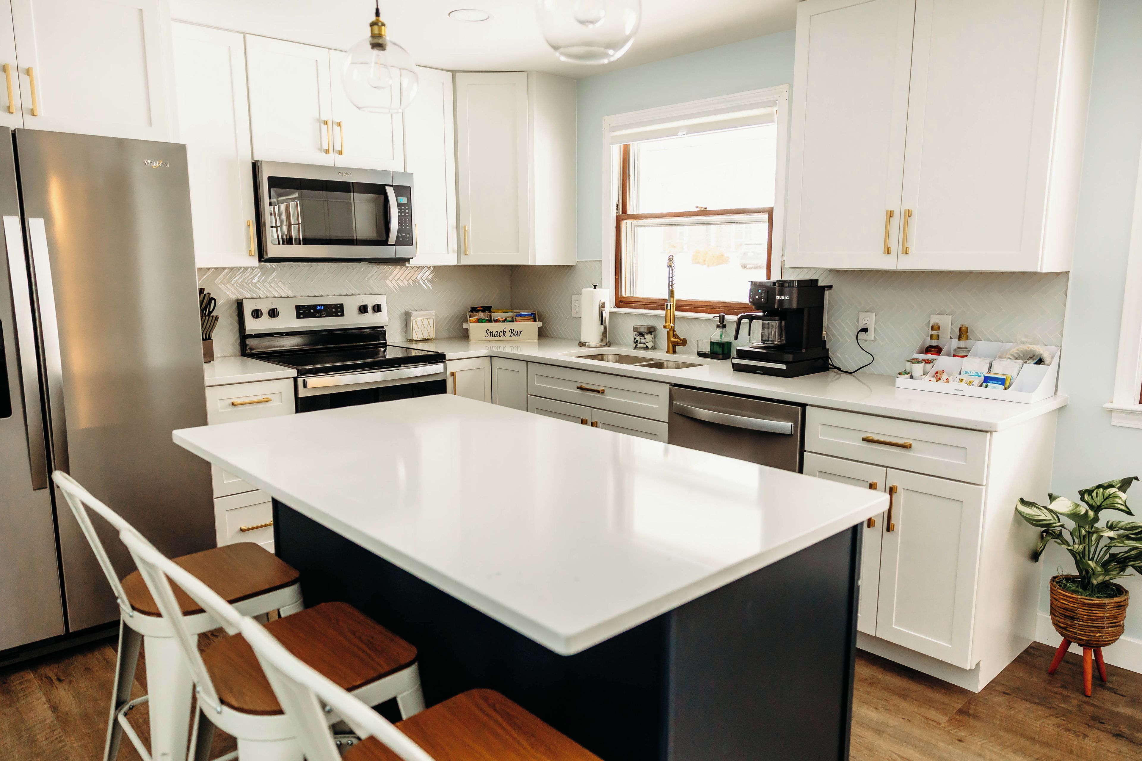 A modern kitchen with white cabinetry, stainless steel appliances, and a central island with bar stools.
