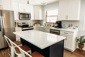 A modern kitchen with white cabinetry, stainless steel appliances, and a central island with bar stools. - Spacious home with hot \tub and lakeview (Mansfield)