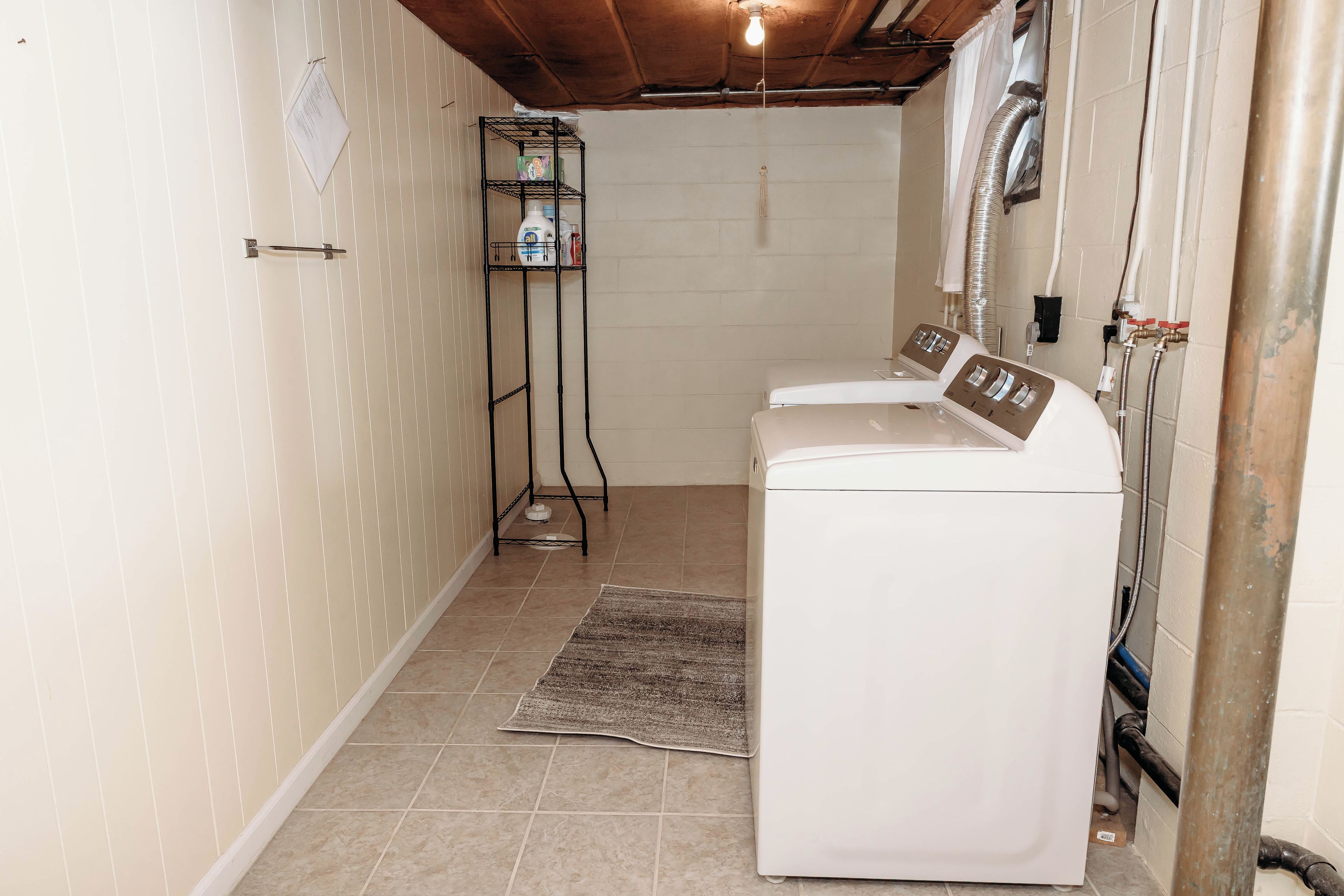 A laundry room with a washing machine, a drying rack, and a small shelf with cleaning supplies.