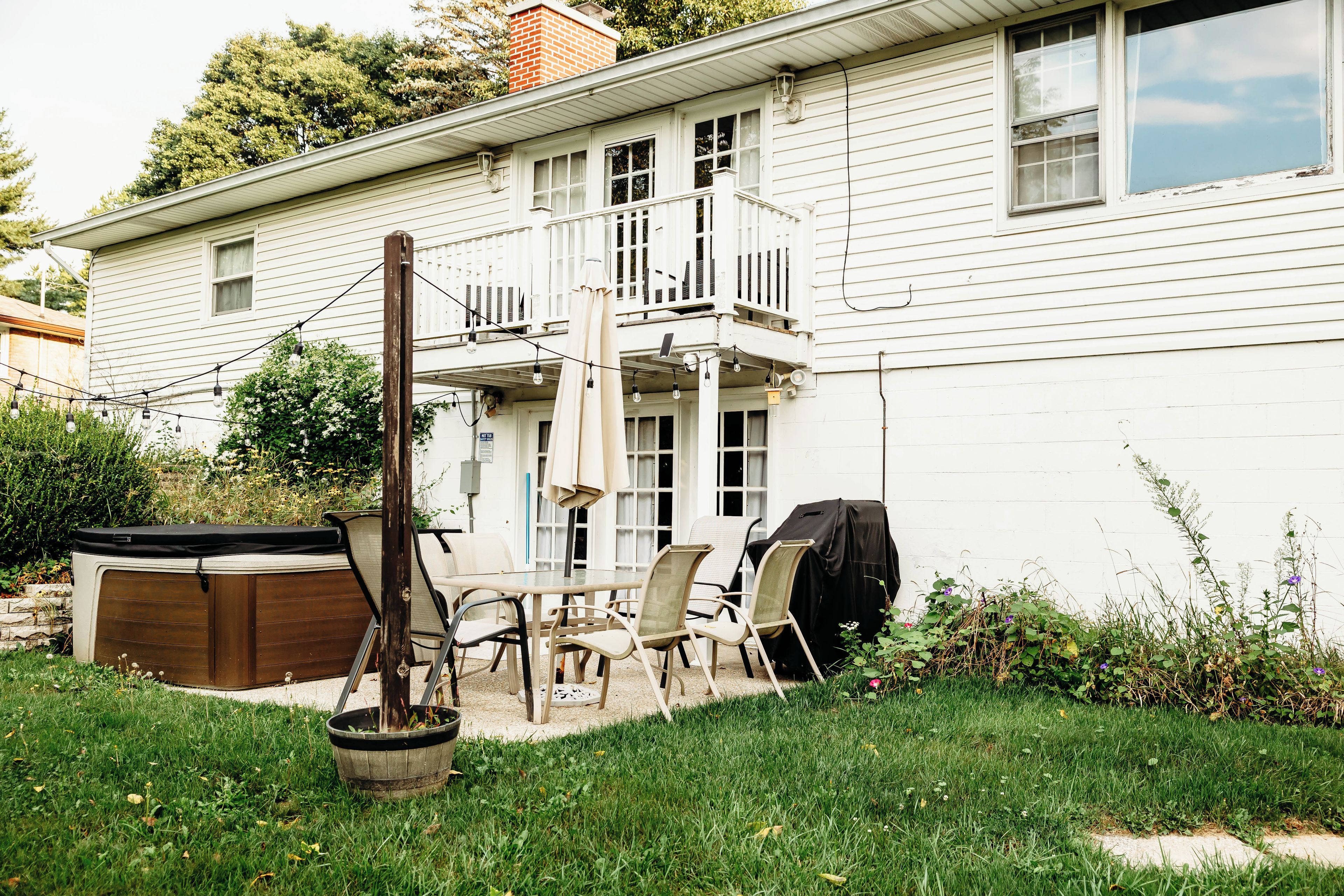 A residential backyard with a patio, outdoor furniture, a hot tub, and a covered grill area.