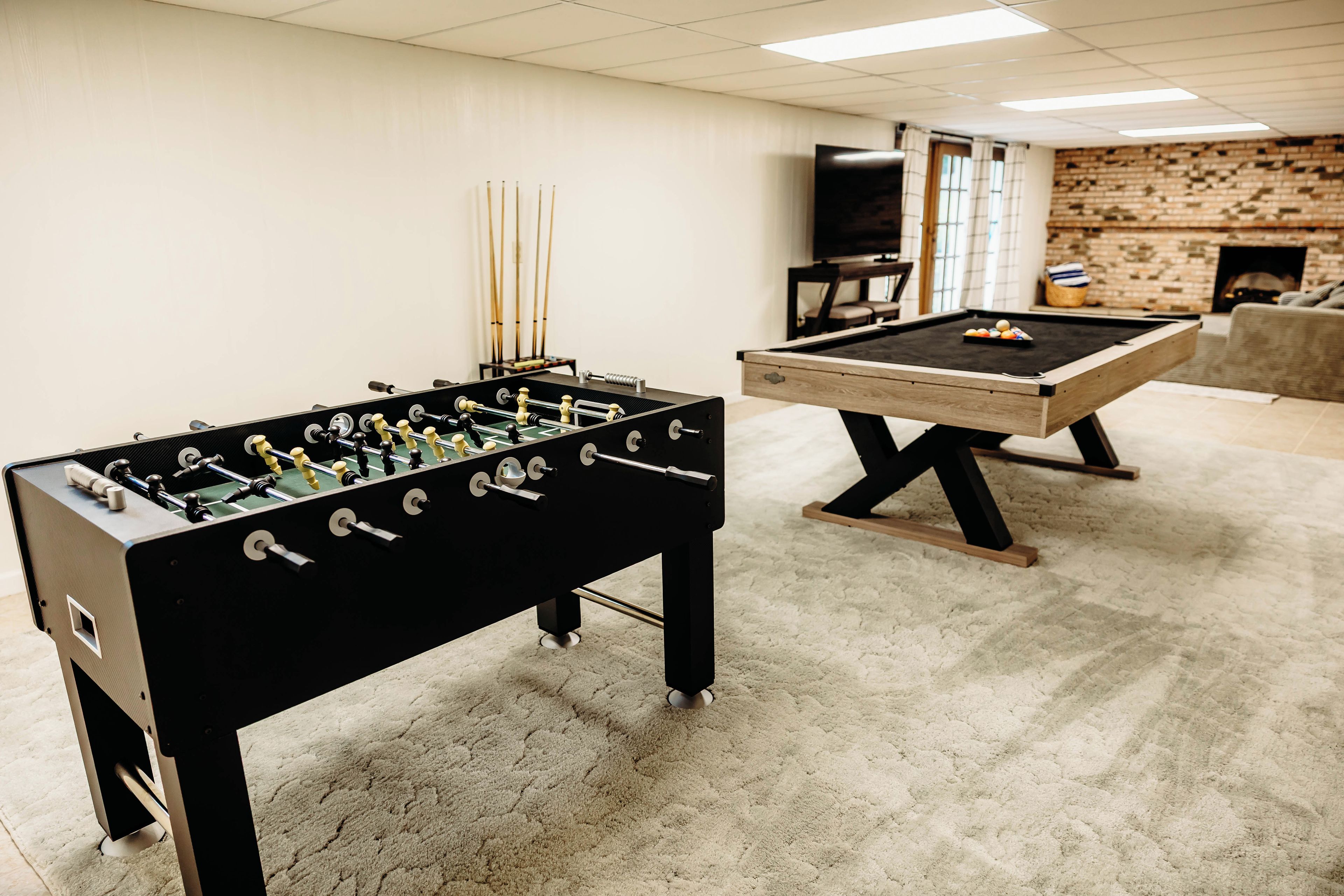 Una habitación con dos mesas de fútbol de mesa, una mesa de billar y una pared de ladrillo.