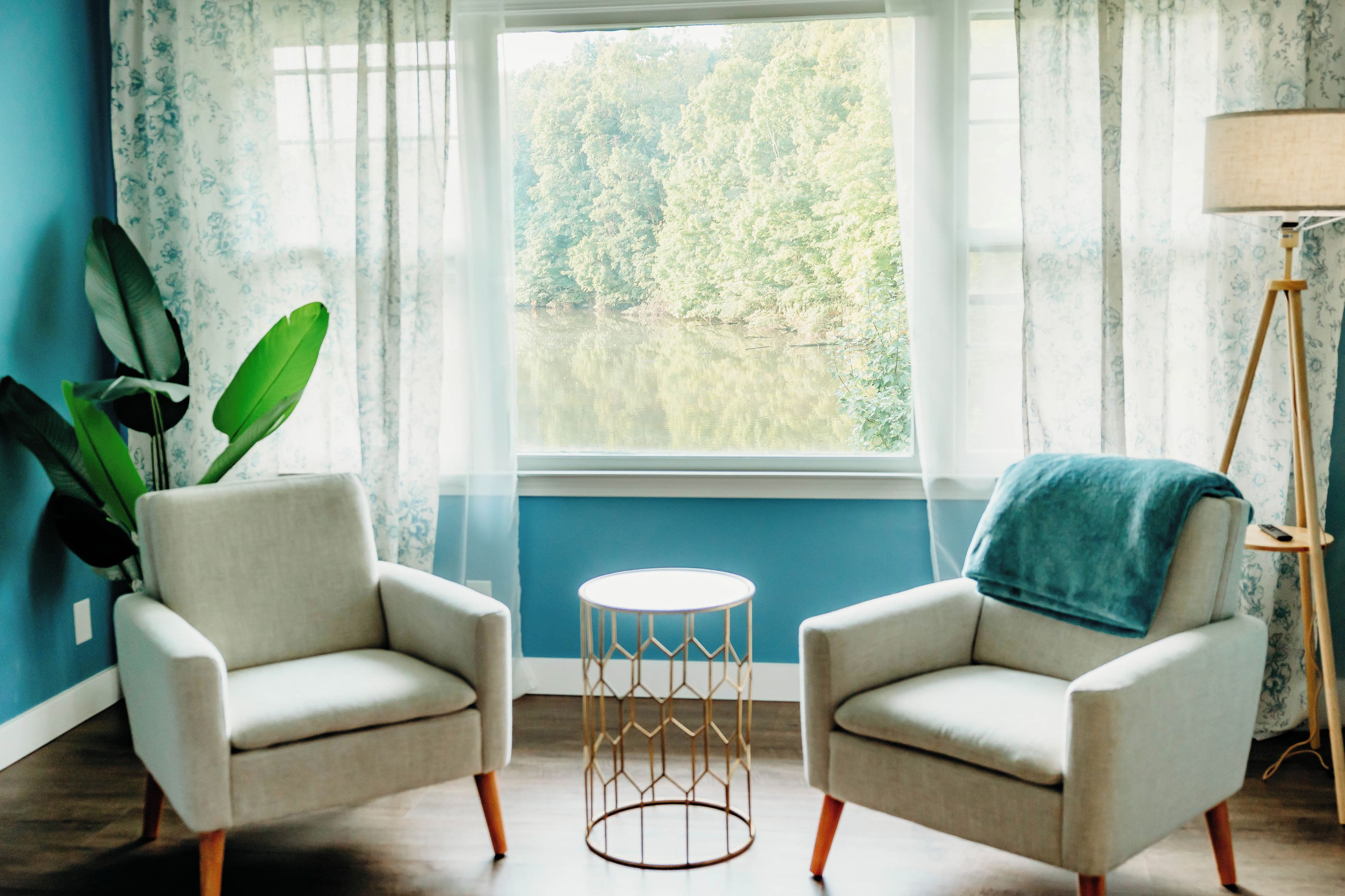 A room with two armchairs, a small round table, and a view of a forest through a window.