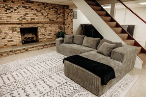 A living room with a brick fireplace, a sectional sofa, a black ottoman, and a patterned rug. - Spacious home with hot \tub and lakeview (Mansfield)