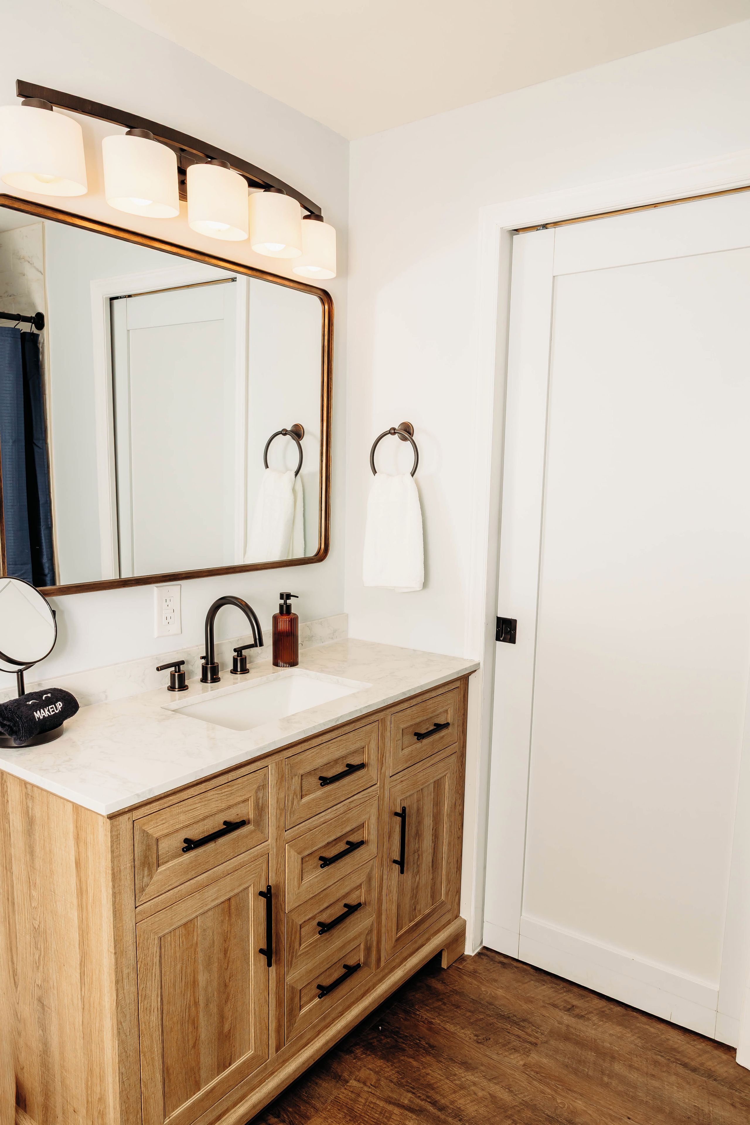 Un baño con tocador de madera, lavamanos, espejo y perchero para toallas.