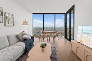 A modern living room with a sofa, coffee table, and a dining area with chairs and a table. - Luxe 1BR Island Getaway in Broadbeach (Broadbeach)