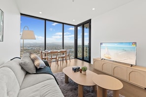 A modern living room with a sofa, a coffee table, and a TV on a wooden cabinet. - Luxe 1BR Island Getaway in Broadbeach (Broadbeach)