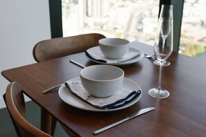A dining table with two white bowls on saucers, a knife, a glass, and a napkin with a blue pattern. - Luxe 1BR Island Getaway in Broadbeach (Broadbeach)