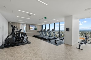 A modern gym with treadmills, stationary bikes, and a TV screen. - Luxe 1BR Island Getaway in Broadbeach (Broadbeach)
