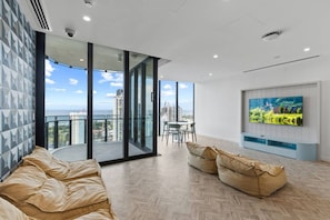 A modern living room with a large TV, a sofa, and a balcony with a city view. - Luxe 1BR Island Getaway in Broadbeach (Broadbeach)