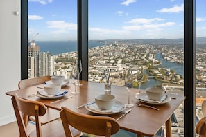 A dining table set with bowls, wine glasses, and cutlery, overlooking a cityscape with a river and buildings. - Luxe 1BR Island Getaway in Broadbeach (Broadbeach)