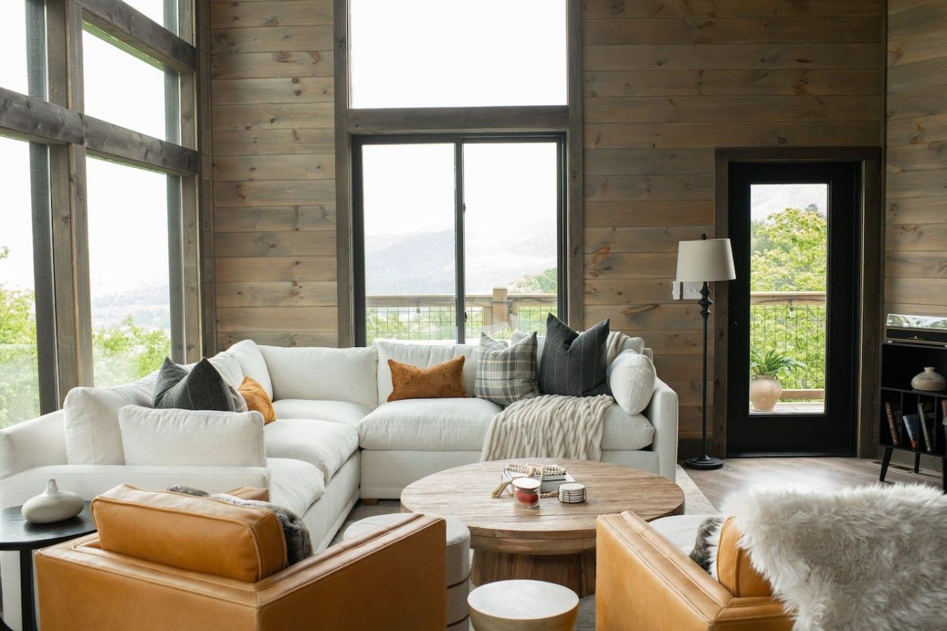 A spacious living room with a large sectional sofa, a round coffee table, and a view of greenery outside.