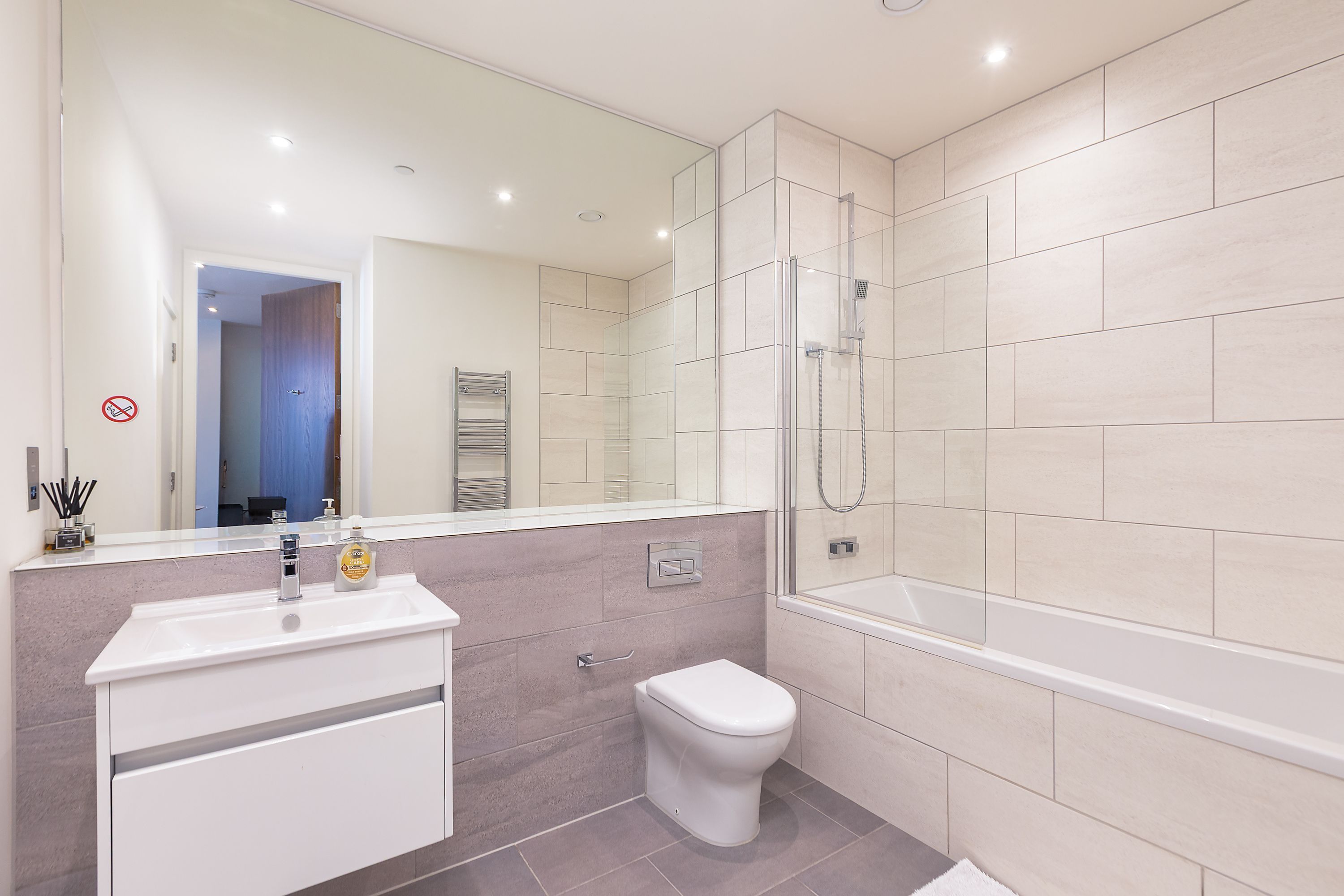 Un bagno moderno con doccia vetrata, lavandino bianco con dispenser di sapone e WC.