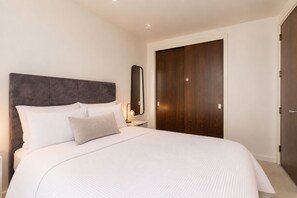 A bedroom with a large bed, a nightstand, a mirror, and a wooden door. - Light-Filled Living in Salford (Salford)