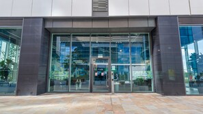 A modern building entrance with glass doors, a sign for 'Green Rooms,' and a tiled pavement. - Light-Filled Living in Salford (Salford)
