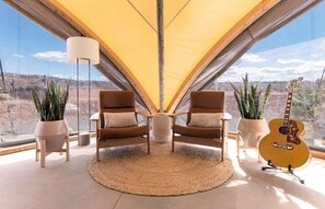 A room with two chairs, a guitar, and potted plants. - Under Canvas Santa Fe (Lamy)