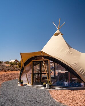 A large, beige, A-frame tent with a door and windows, set on a gravel surface with potted plants outside. - Under Canvas Santa Fe (Lamy)