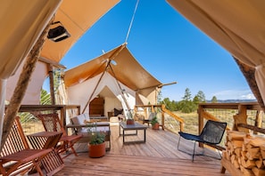 A tented accommodation with a wooden deck, outdoor seating, and a view of the surrounding landscape. - Under Canvas Santa Fe (Lamy)