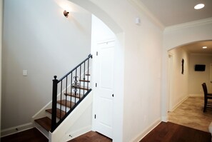 A hallway with a staircase, a white door, and a flat-screen TV mounted on the wall.