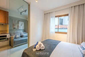 A hotel room with a bed, a desk, a chair, and a window with curtains. - Apt. Well Located w/ Garage in Condo. Hes0109 (Salvador)
