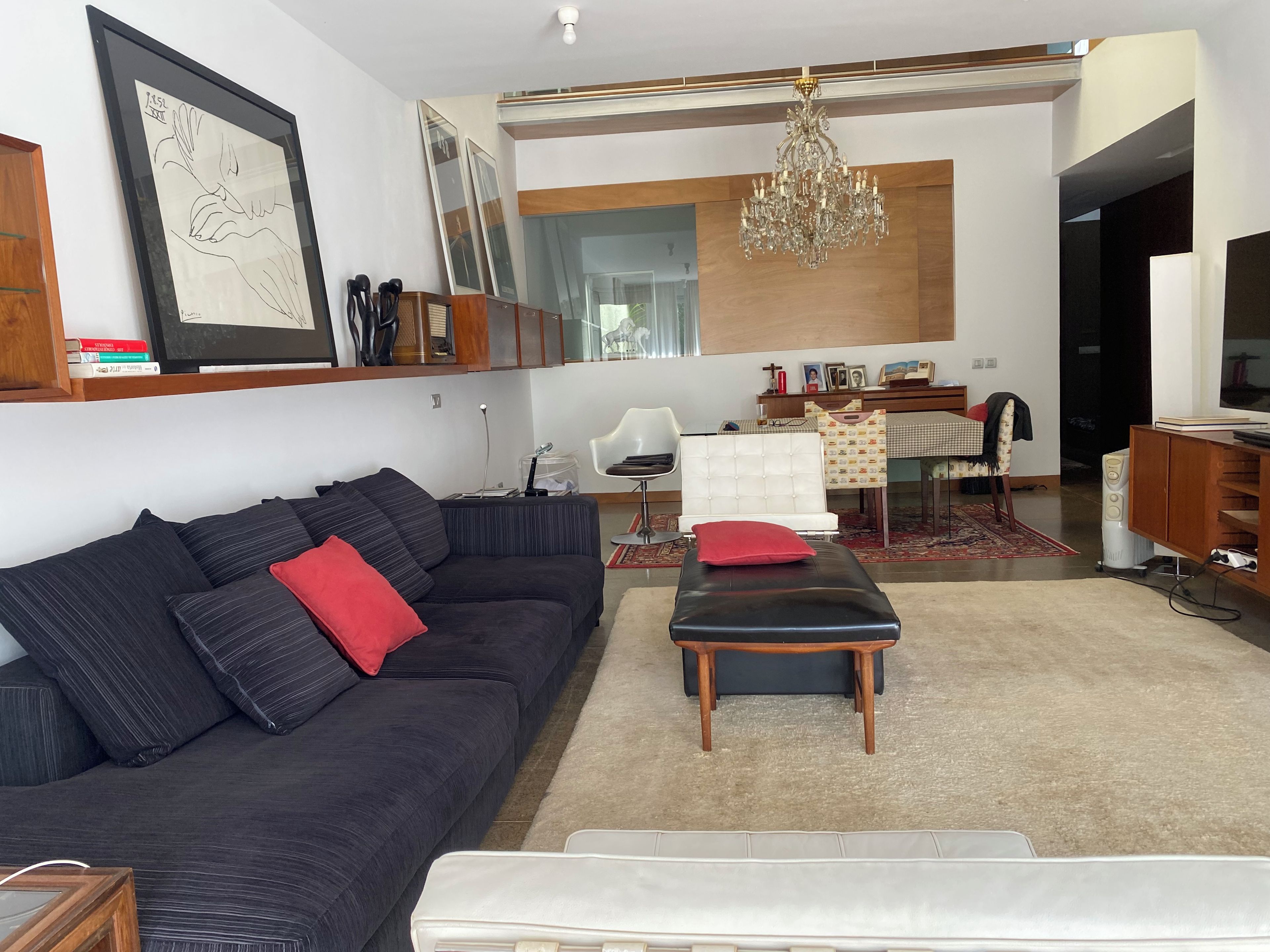 Een moderne woonkamer met een donkere bank, een witte fauteuil, een houten salontafel en een kroonluchter.