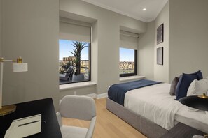 Un dormitorio moderno con una cama, un escritorio y dos ventanas con vistas a la ciudad.