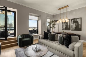 Una sala de estar moderna con un sofá, una mesa redonda de centro y vistas de la ciudad a través de grandes ventanales.