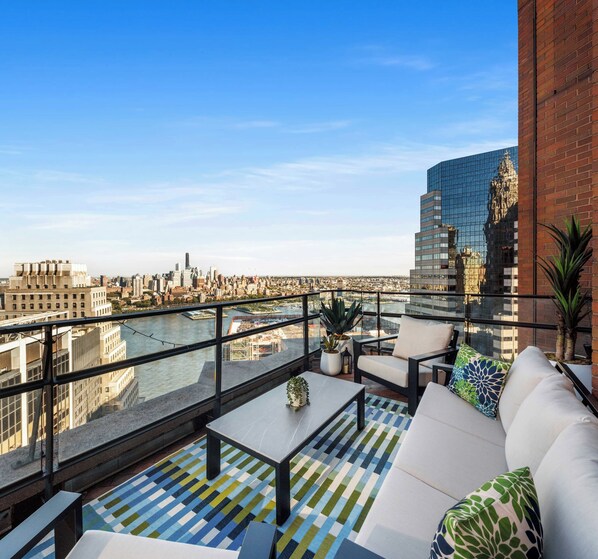 Una terraza en la azotea con vistas a un horizonte urbano, un río y edificios modernos.