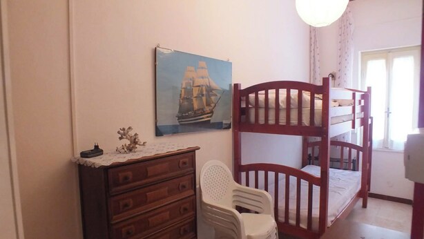 Una habitación con literas, un aparador, una silla, un cuadro en la pared y una ventana con cortinas.