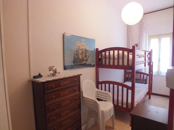 Ein Zimmer mit einem Etagenbett, einem Schminktisch, einem Stuhl, einem Bild an der Wand und einem Fenster mit Vorhängen.