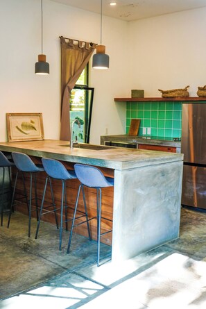 A kitchen with a central island, bar stools, a refrigerator, and a green tiled backsplash. - Fresh Reno, 5 Min to Beach: Private Compound for Groups of 15 (Nosara)