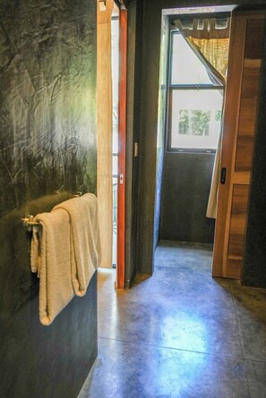 A hallway with a towel hanging on a wall, a door leading to a room, and a concrete floor. - Fresh Reno, 5 Min to Beach: Private Compound for Groups of 15 (Nosara)