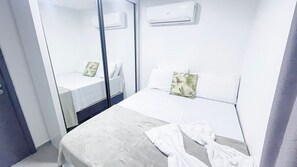 A hotel room with a bed, a bedside table, a mirror, and an air conditioning unit. - Residencial Di Mare - Porto de Galinhas (Ipojuca)