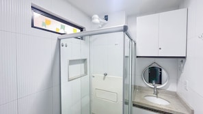 A bathroom with a glass shower enclosure, a white sink with a mirror, and a white cabinet above the sink. - Residencial Di Mare - Porto de Galinhas (Ipojuca)