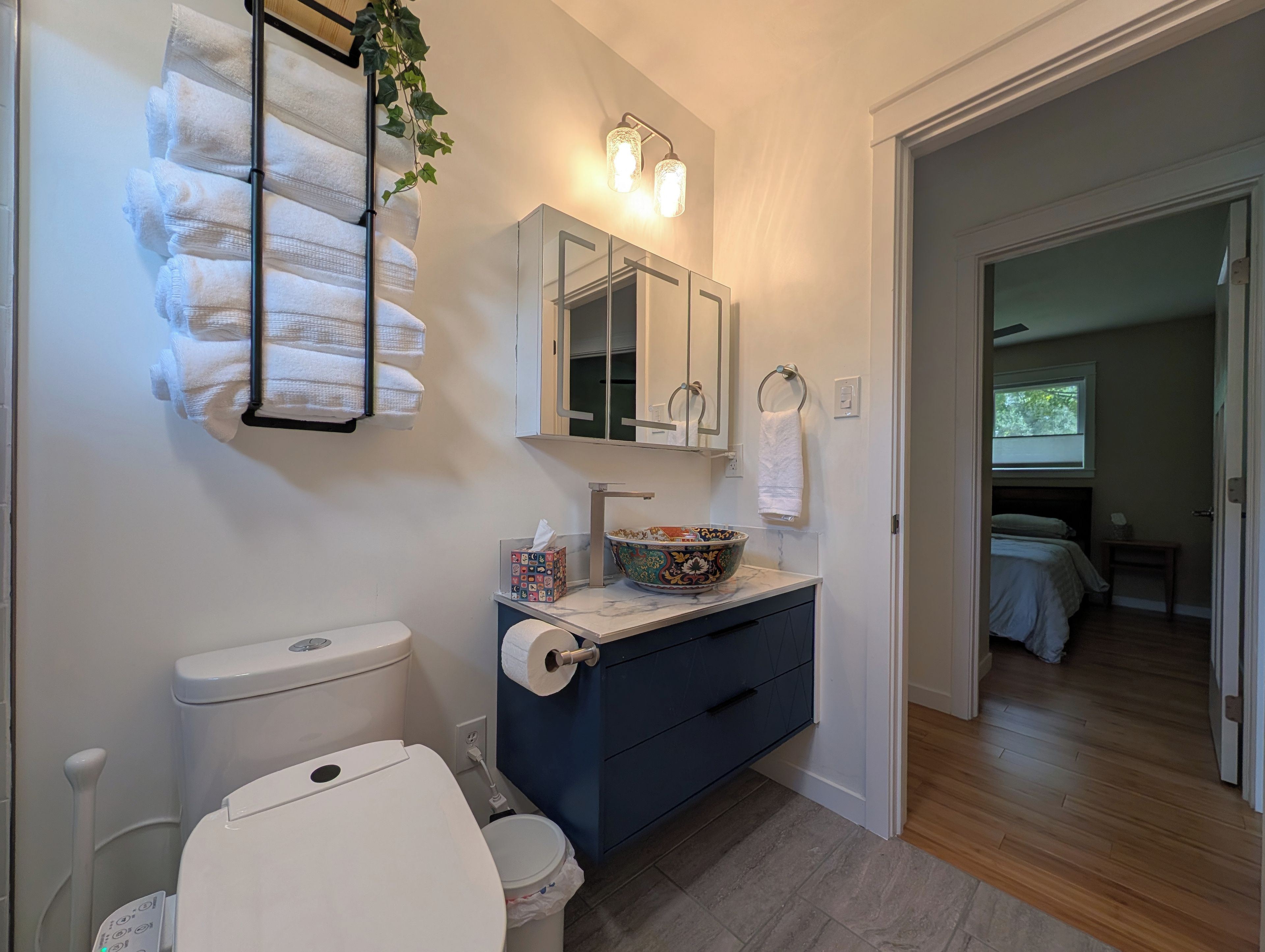 Ein Badezimmer mit Toilette, Waschbecken und Spiegel. Handtücherhalter mit Handtüchern, Toilettenpapierhalter und eine dekorative Schale auf dem Waschbecken.