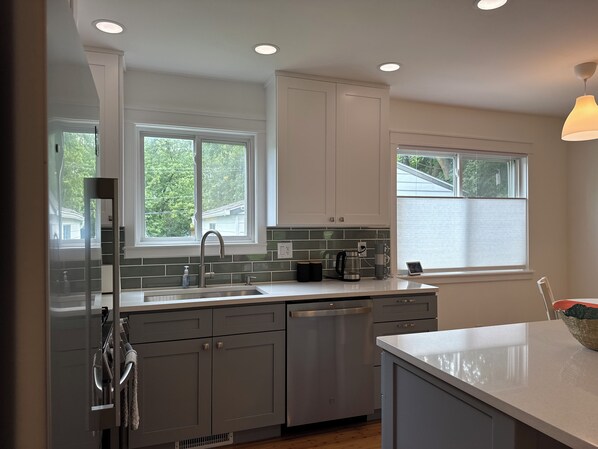 A modern kitchen with white cabinets, a stainless steel dishwasher, and a window with a view of greenery outside.