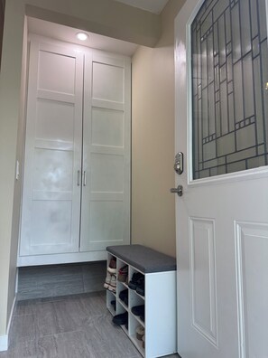 A hallway with a white door, a bench with shoe storage, and a shoe rack.