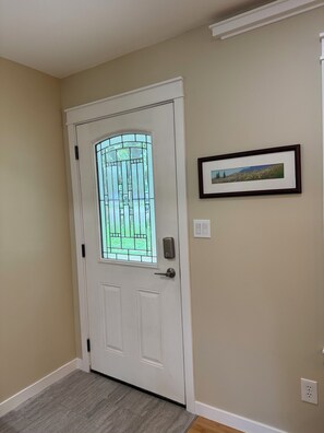 A white door with a glass panel, a picture frame on the wall, and a light switch. - Cozy 3 bed Craftsman Retreat, 10 Min from the Big House (Ann Arbor)